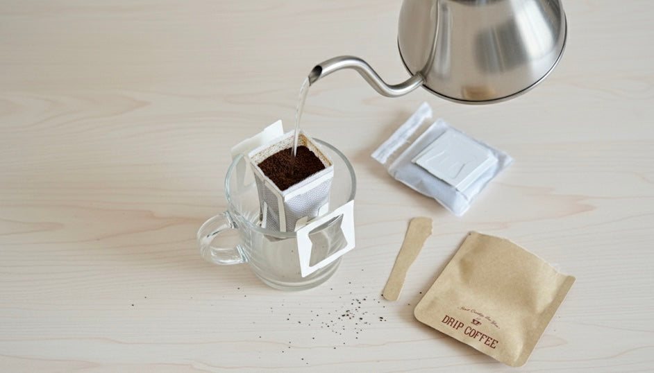 A kettle pouring hot water into a hanging drip coffee pouch